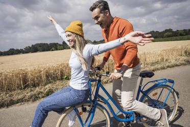 Happy man and woman enjoying bicycle ride in front of field - UUF29668