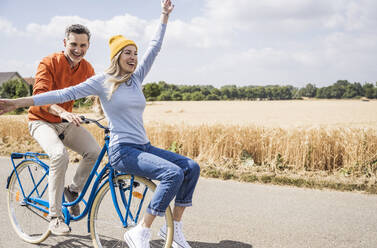 Happy mature man giving bicycle ride to woman in front of field - UUF29669