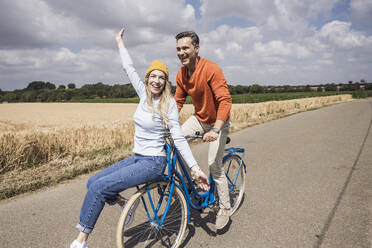 Fröhlicher reifer Mann, der einer Frau vor einem Feld eine Fahrradtour ermöglicht - UUF29670