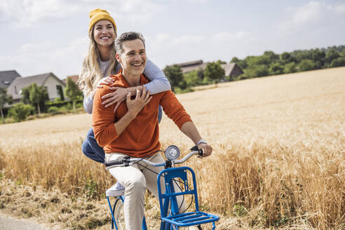 Verliebtes Paar beim Fahrradfahren vor einem Feld - UUF29675