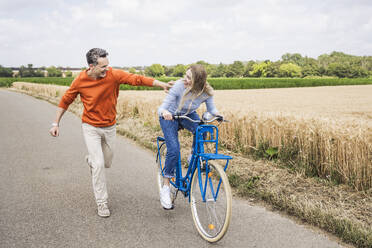 Glückliche Frau auf dem Fahrrad mit einem Mann, der auf der Straße läuft - UUF29689