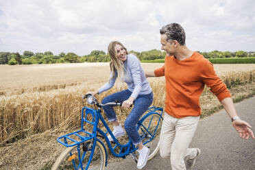 Fröhliche Frau auf dem Fahrrad mit einem Mann, der auf der Straße läuft - UUF29690