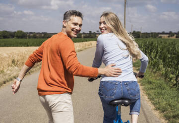 Happy woman riding bicycle and enjoying with man on road - UUF29691