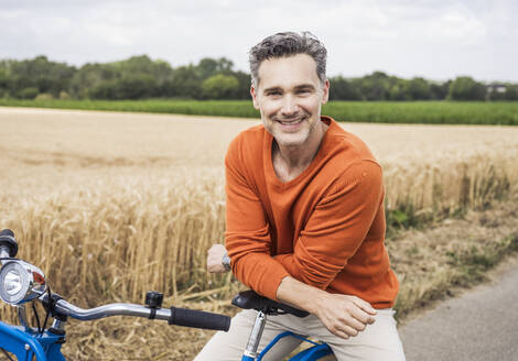 Lächelnder reifer Mann auf dem Fahrrad sitzend - UUF29701