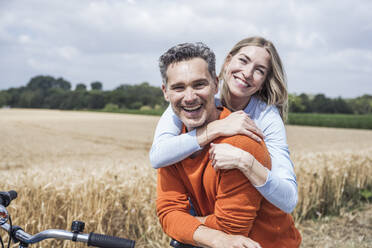 Glückliches Paar sitzt auf einem Fahrrad in der Nähe eines Feldes - UUF29703