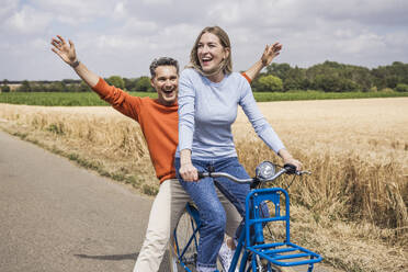 Glücklicher Mann hat Spaß mit einer Frau, die in der Nähe eines Feldes Fahrrad fährt - UUF29705