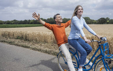 Mature man enjoying bicycle ride with woman near field - UUF29707