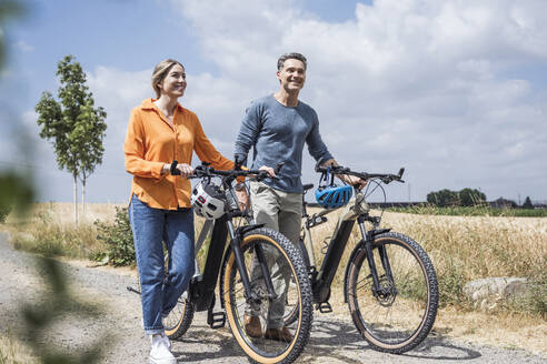 Couple wheeling with bicycles on road near field - UUF29708