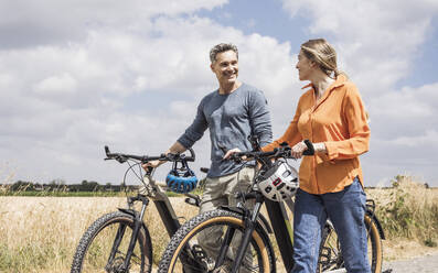 Smiling couple walking with bicycles near field - UUF29709