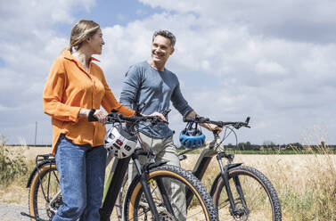 Smiling man looking at woman wheeling bicycle near field - UUF29710