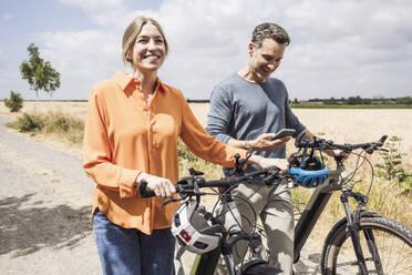 Lächelnde Frau auf einem Fahrrad mit einem Mann, der ein Smartphone benutzt - UUF29714