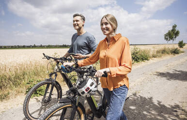 Man holding smart phone by woman wheeling bicycle on road - UUF29715