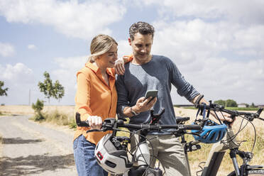 Couple with bicycles sharing smart phone standing on road - UUF29716