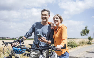 Glücklicher Mann mit Smartphone, der mit einer Frau mit Fahrrad steht - UUF29718