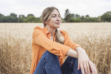 Smiling woman with eyes closed sitting at field - UUF29737