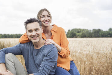 Smiling woman sitting with man at field - UUF29738