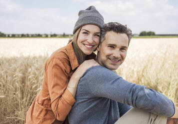 Smiling woman wearing knit hat sitting with man at field - UUF29741