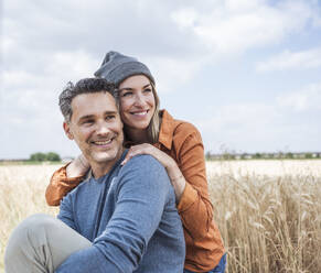 Happy couple enjoying leisure time sitting at field - UUF29745