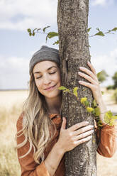 Smiling woman with eyes closed embracing tree - UUF29751