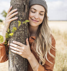 Lächelnde Frau umarmt Baum auf einem Feld - UUF29752