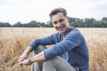 Smiling mature man sitting in field - UUF29771