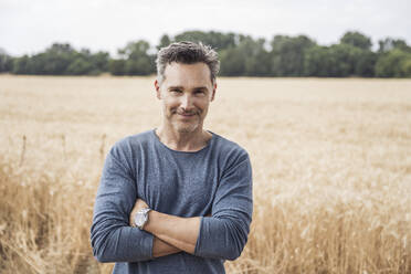 Smiling man standing with arms crossed in front of field - UUF29778