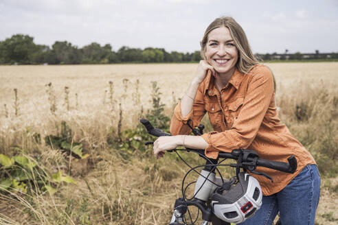 Smiling woman leaning on bicycle at field - UUF29781