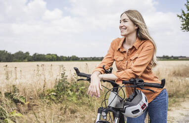 Glückliche reife Frau lehnt auf Fahrrad in der Nähe von Feld - UUF29782