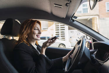 Glückliche Geschäftsfrau, die im Auto mit ihrem Smartphone telefoniert - PNAF05872