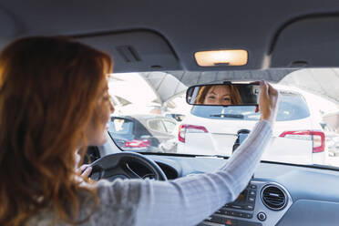 Rothaarige Frau beim Einstellen des Rückspiegels im Auto - PNAF05878