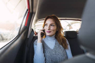 Lächelnde Frau, die im Auto mit ihrem Smartphone telefoniert - PNAF05880