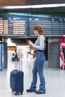 Rothaarige Frau benutzt Smartphone am Flughafen - PNAF05888