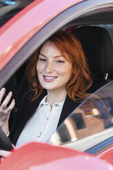 Lächelnde rothaarige Geschäftsfrau in rotem Auto sitzend - PNAF05923
