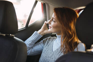 Glückliche rothaarige Frau, die im Auto mit einem Smartphone telefoniert - PNAF05925