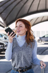 Happy woman talking on mobile phone at parking lot - PNAF05928