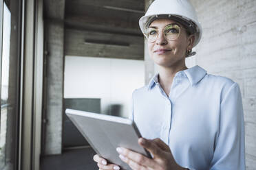 Smiling engineer wearing hardhat standing with tablet PC - UUF29786