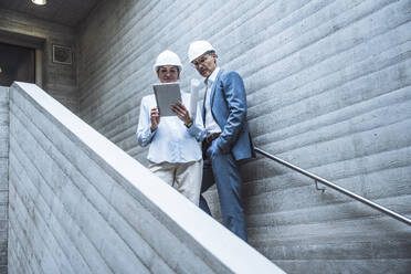 Businessman and businesswoman discussing over tablet PC on staircase - UUF29787