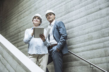 Thoughtful architects standing with tablet PC on staircase - UUF29788