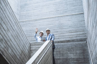 Architect gesturing and having discussion with colleague on staircase - UUF29796