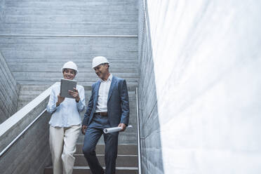 Happy architect using tablet PC and discussing with colleague on staircase - UUF29799