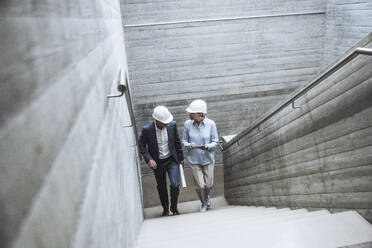 Architects wearing hardhat moving up on staircase - UUF29806