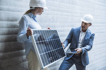 Geschäftsmann und Geschäftsfrau mit Schutzhelm diskutieren über ein Solarpanel - UUF29816