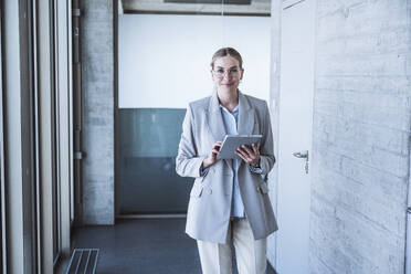 Smiling businesswoman with tablet PC in office corridor - UUF29827