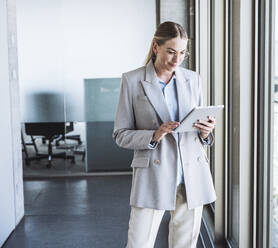 Smiling businesswoman using tablet PC standing in office - UUF29830