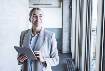 Happy businesswoman standing with tablet PC in office - UUF29832