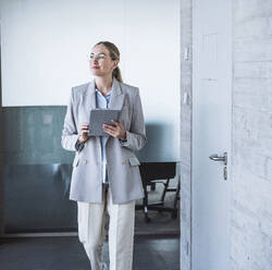 Smiling businesswoman walking with tablet PC in office - UUF29833