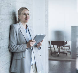 Nachdenkliche Geschäftsfrau stehend mit Tablet-PC im Büro - UUF29837
