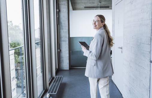 Glückliche Geschäftsfrau, die mit einem Tablet-PC im Korridor spazieren geht - UUF29839