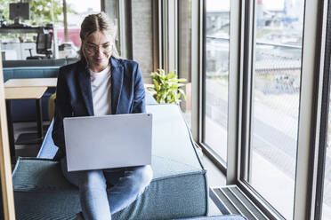 Smiling businesswoman working on laptop in office - UUF29840