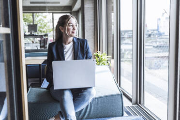 Thoughtful businesswoman sitting with laptop in office - UUF29841